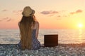 Girl in a hat sits on the beach, near a laptop. Sea at sunset