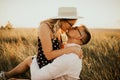 A girl in hat sits in hands guy on ground in middle of tall grass in meadow