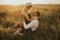 A girl in hat sits in hands guy on ground in middle of tall grass in meadow