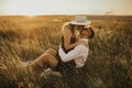 A girl in hat sits in hands guy on ground in middle of tall grass in meadow