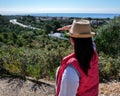 A brunette girl in a hat is standing on a mountain and looking at the road away Royalty Free Stock Photo