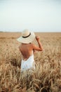 The girl in a hat stands in a field of ripe wheat in the sunset light. Sunset sun. Walking in the wheat field Royalty Free Stock Photo
