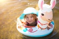 Girl in a hat swimming in the river with inflatable circle in the shape of a lama. Inflatable alpaca for a child. Sea with a sandy Royalty Free Stock Photo