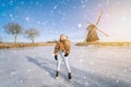 Girl having fun on ice in typical dutch landscape with windmill. Woman ice skating on rink outdoors in sunny snowy day Royalty Free Stock Photo