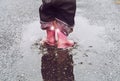 Girl having fun jumping in water puddle on wet street wearing rain boots with reflective detail fabric stripes shining.
