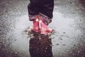Girl having fun jumping in water puddle on wet street wearing rain boots with reflective detail fabric stripes shining.