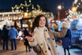 Girl having fun with sparklers on christmas decoration lights street. Young happy smilin Woman wearing stylish knitted scarf, coat