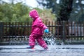 Girl is having fun in water on street in cold autumn day, girls splashing water in rain Royalty Free Stock Photo