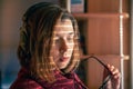 A girl with headphones behind a laptop in the sunlight, through the blinds. Royalty Free Stock Photo