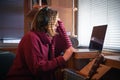 A girl with headphones behind a laptop in the sunlight, through the blinds. Royalty Free Stock Photo