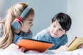 Girl in headphones and boy using digital tablets while lying on bed Royalty Free Stock Photo