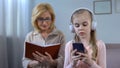 Girl in headphones listening to music and grandma reading book, generation gap Royalty Free Stock Photo