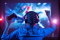 Girl in headphones plays a video game on the big TV screen. Gamer with a joystick. Online gaming with friends, win, prize. Fun Royalty Free Stock Photo