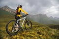 A girl in a helmet and with a backpack with a bicycle stands against the backdrop of epic mountains and rocks and a Royalty Free Stock Photo