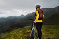 A girl in a helmet and with a backpack with a bicycle stands against the backdrop of epic mountains and rocks and cloudy Royalty Free Stock Photo