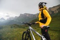 A girl in a helmet and with a backpack with a bicycle stands against the backdrop of epic mountains and rocks and cloudy Royalty Free Stock Photo