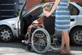 Girl helping woman on wheelchair getting into a car