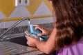 Girl on her back, cleaning a glass with a scourer in the kitchen sink. Helping with the housework