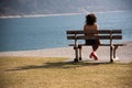 A girl sitting over her shoulder on a wooden bench looks at a mountain lake. Royalty Free Stock Photo