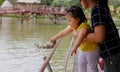 A girl and her mother feeding fish in a pond using food pellet