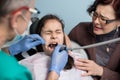 Girl with her mother on the first dental visit. Senior pediatric dentist drilling patient tooth at the dental office Royalty Free Stock Photo