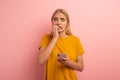 Girl with her smartphone. Scared and afraid expression. Pink background