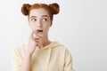 Girl hesitates while having idea in her mind. Portrait of nervous attractive ginger woman with two buns hairstyle