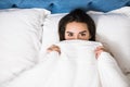 Girl hides her face in bed at home. Cheerful girl in bed hiding her face under the blanket. Teenage girl lying under a blanket. Wo