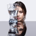 Girl hides her face behind a glass vase. Beauty portrait of young woman at the mirror table