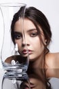 Girl hides her face behind a glass vase. Beauty portrait of young woman at the mirror table Royalty Free Stock Photo