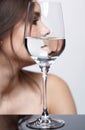 Girl hides her face behind a glass glass of water. Beauty portrait of young woman on gray background