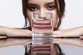 Girl hides her face behind a glass with water. Optical distortion portrait of young woman at the mirror table Royalty Free Stock Photo