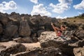 A girl on a high stone in the fresh air goes in for sports. She does an exercise from the Pilates teaser.