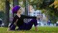 Girl in hijab muslim woman sports lady female yogi sitting in city park on grass lawn holds foot under arm doing Royalty Free Stock Photo