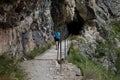 A girl on a hike crosses a wooden bridge on a path that enters the tunnel carved into the mountain.