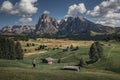 Girl hiking along meadows with wooden cabins at Alpe di Siusi during summer with view to mountains of Plattkofel and Langkofel in Royalty Free Stock Photo