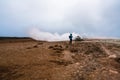 Girl with hiking gear infront of sulphur steam vents in Iceland during heavy cold wind. Mineral rich and textured muddy ground inf