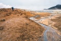 Girl with hiking gear walking towards sulphur steam vents in Iceland during heavy cold wind.