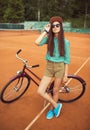 Girl hipster standing with magenta bike on the tennis court