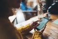 Girl hold in hands yellow mobile phone, person type message on empty screen smartphone in sun cafe, relax tourist travels planning Royalty Free Stock Photo