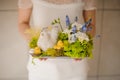 Girl holding a beautiful spring composition with toy chiken and white and blue flowers