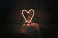 Girl holding big luminous heart over dark background, waiting for love in Valentine Day