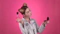 Girl holding a brush in her hand and powdering her face. Pink background. Slow motion