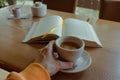 Girl holding coffee cup with open book on background. Cup of coffee and book with bookmark. Cozy morning time. Leisure concept. Royalty Free Stock Photo