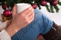 Girl holding cup of coffee in hand at legs with warmers and Christmas tree in the background Royalty Free Stock Photo