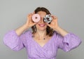 Girl holding donuts like glasses and smiling in purple dress on gray background