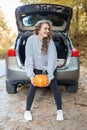 Girl is holding freshly picked organic orange pumpkin near car. Woman is having fun. Autumn season