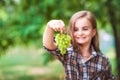 The girl is holding a grapes, a focus on green grapes. Beautiful little farmer girl eating organic grapes. The concept of harvest.