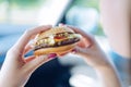 Girl holding a hamburger in her hands sitting in a car. Unhealt