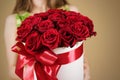 Girl holding in hand rich gift bouquet of 21 red roses. Composition of flowers in a white hatbox. Tied with wide red ribbon and b